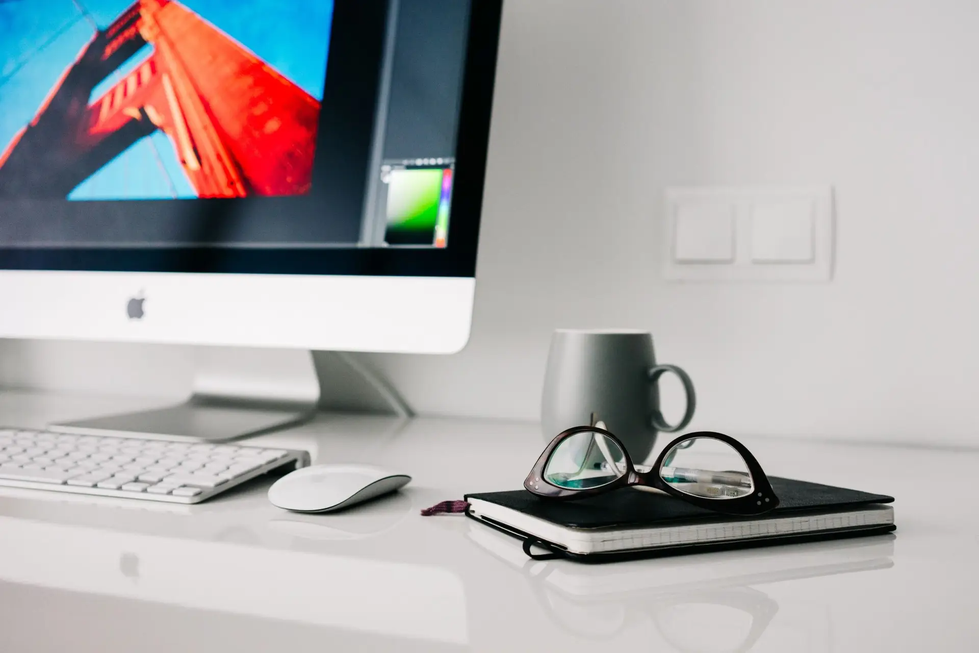 Stylish office workspace featuring a desktop computer, glasses, and notebook.